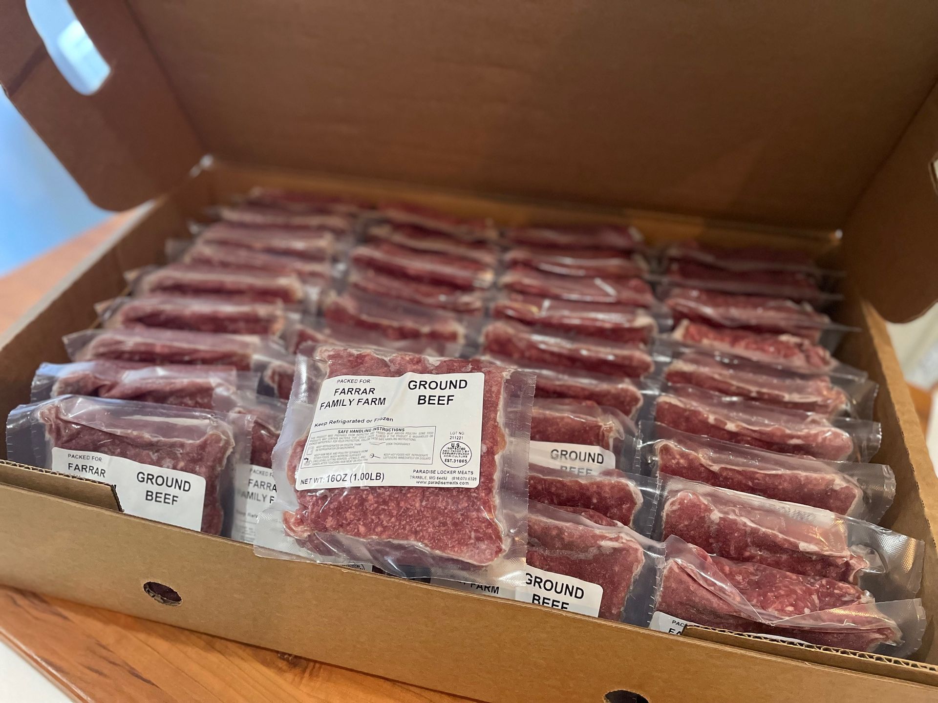 Una caja de cartón llena de carne cruda de res, envasada individualmente y sellada al vacío. Cada paquete está etiquetado y cuidadosamente organizado.