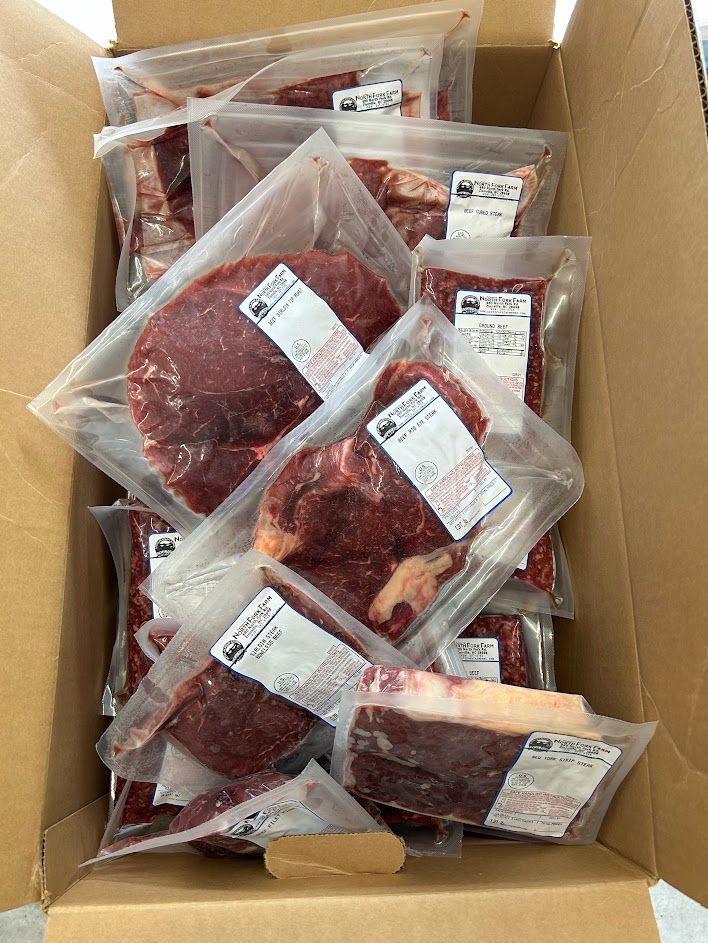 Una caja de cartón rebosante de paquetes sellados al vacío de carne roja cruda.