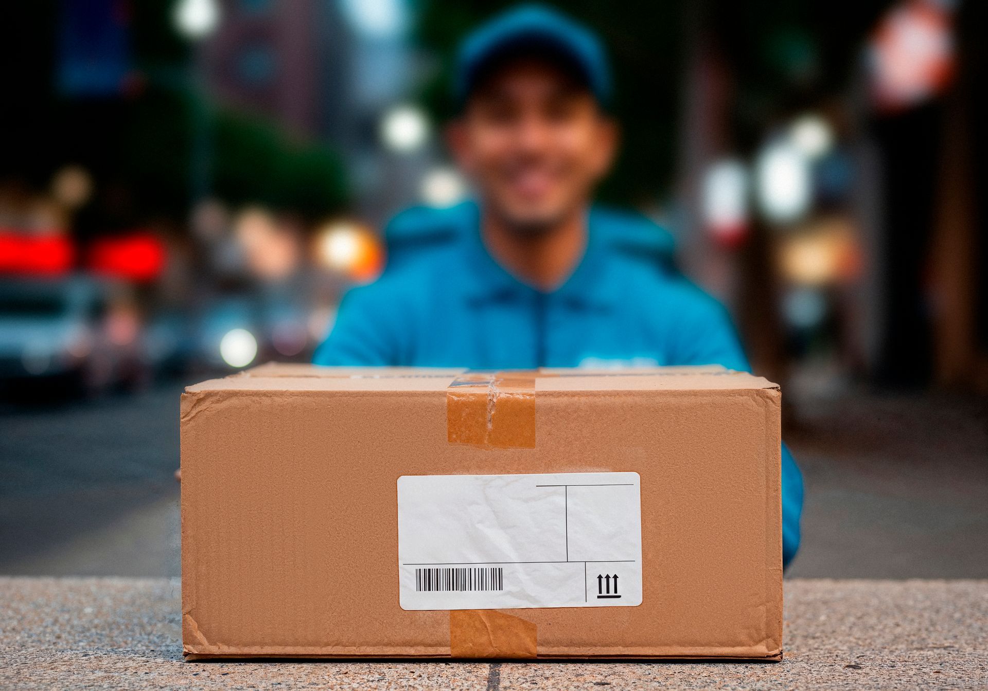 Repartidor entregando un paquete en una caja de cartón en la calle, con fondo urbano desenfocado.