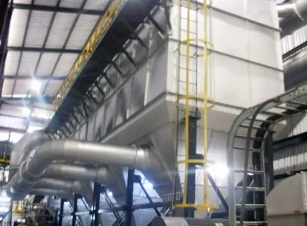 Gran colector de polvo industrial con conductos metálicos y escalera de seguridad, en el interior de una fábrica.