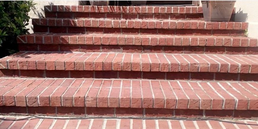 A person is using a high pressure washer to clean a brick wall.