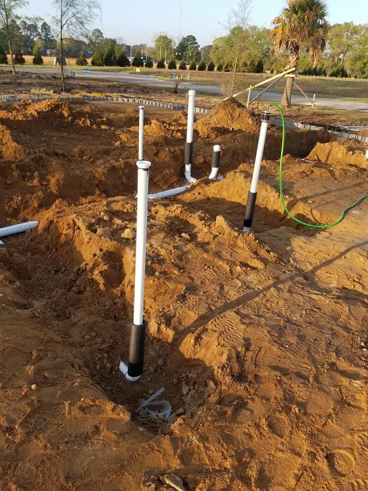 A bunch of pipes are laying in the dirt on a construction site.