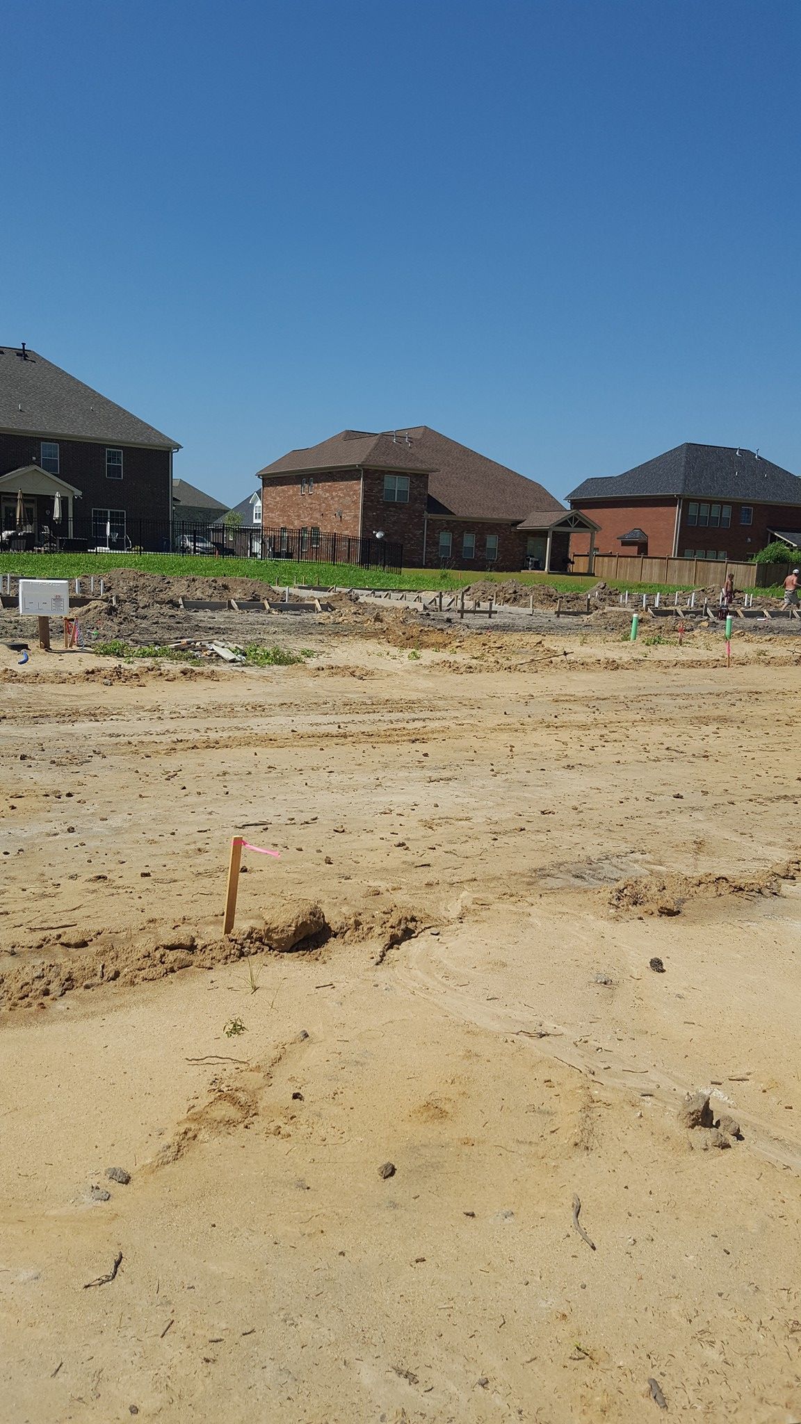 A dirt field with houses in the background on a sunny day