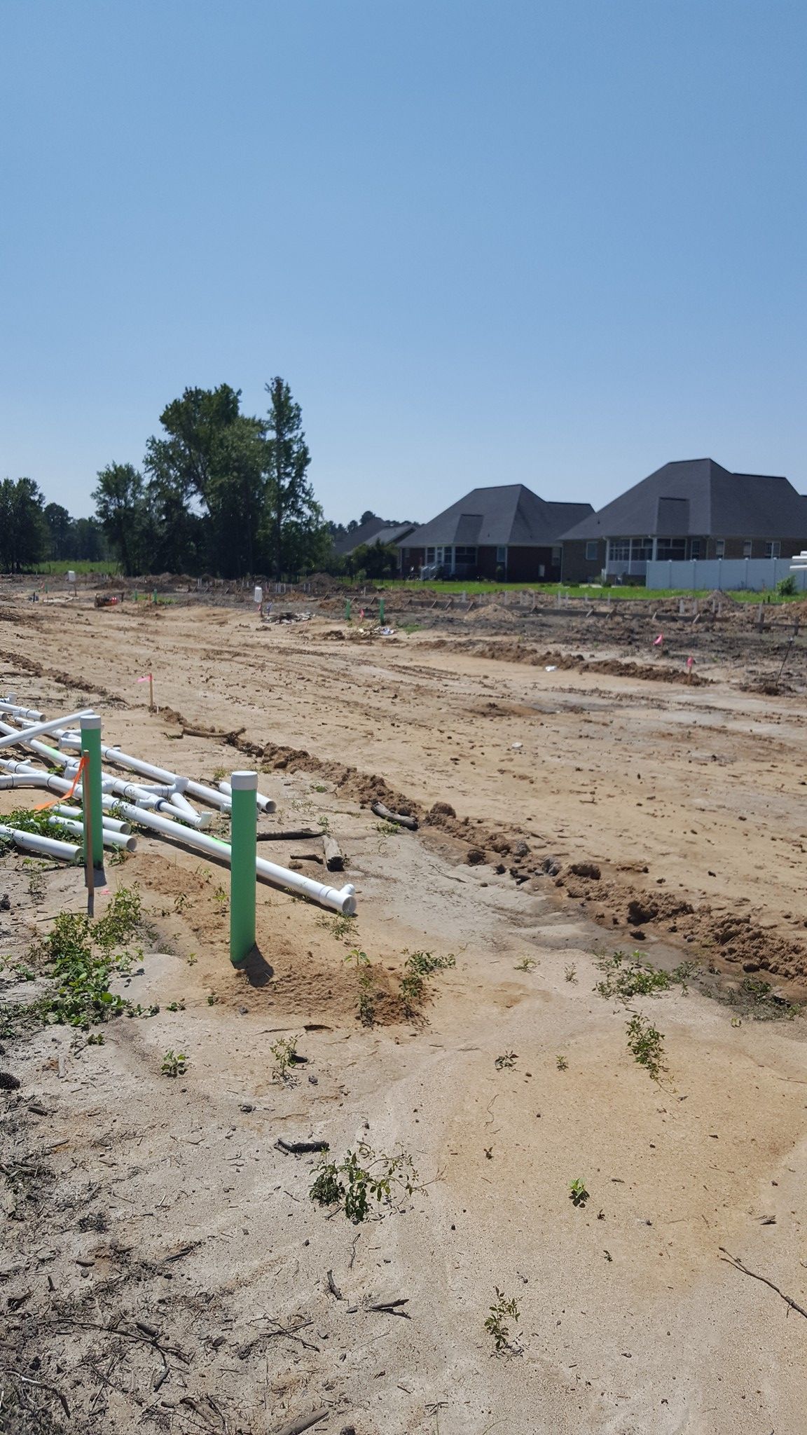A dirt field with a fence and houses in the background.