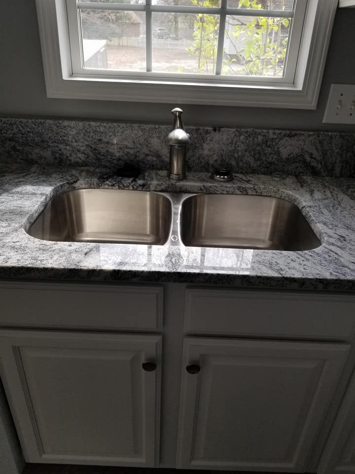 A kitchen sink is sitting on top of a granite counter next to a window.