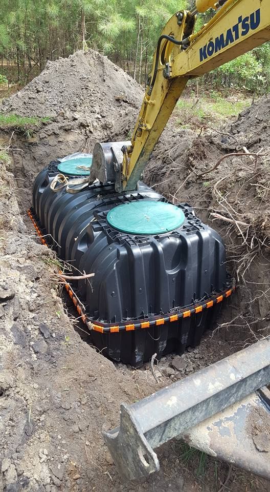 A yellow excavator is digging a septic tank in the dirt.