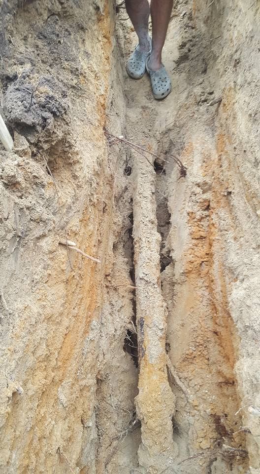 A person is standing in a dirt trench next to a pipe.
