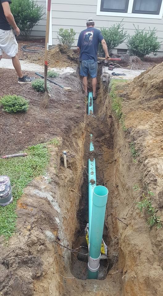 A man is standing in a trench next to a green pipe.