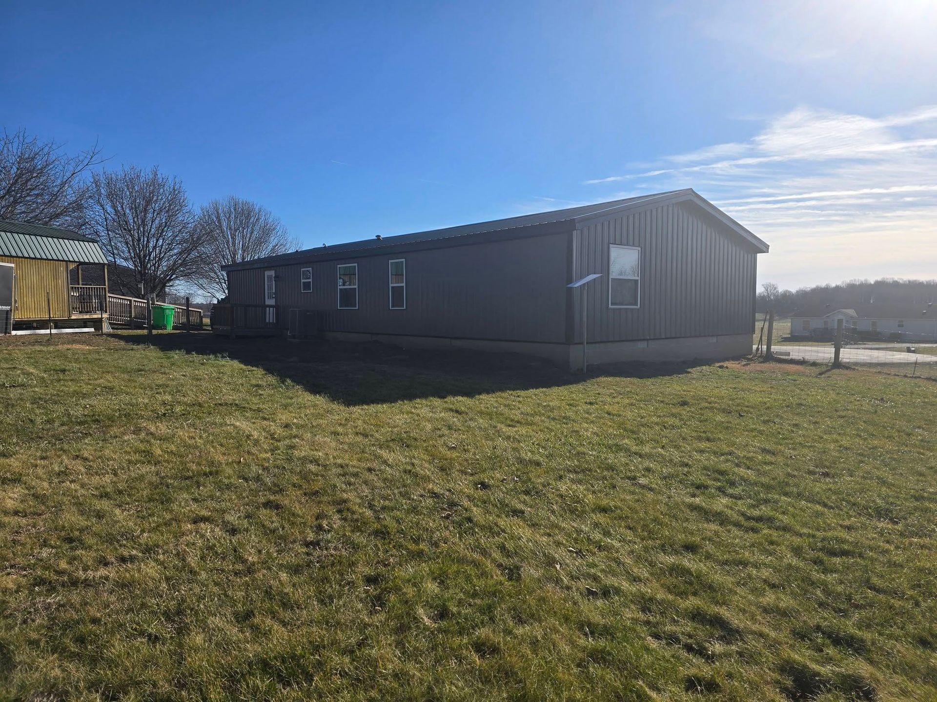 A gray manufactured home sits on a grassy hill under a clear blue sky on a sunny day.