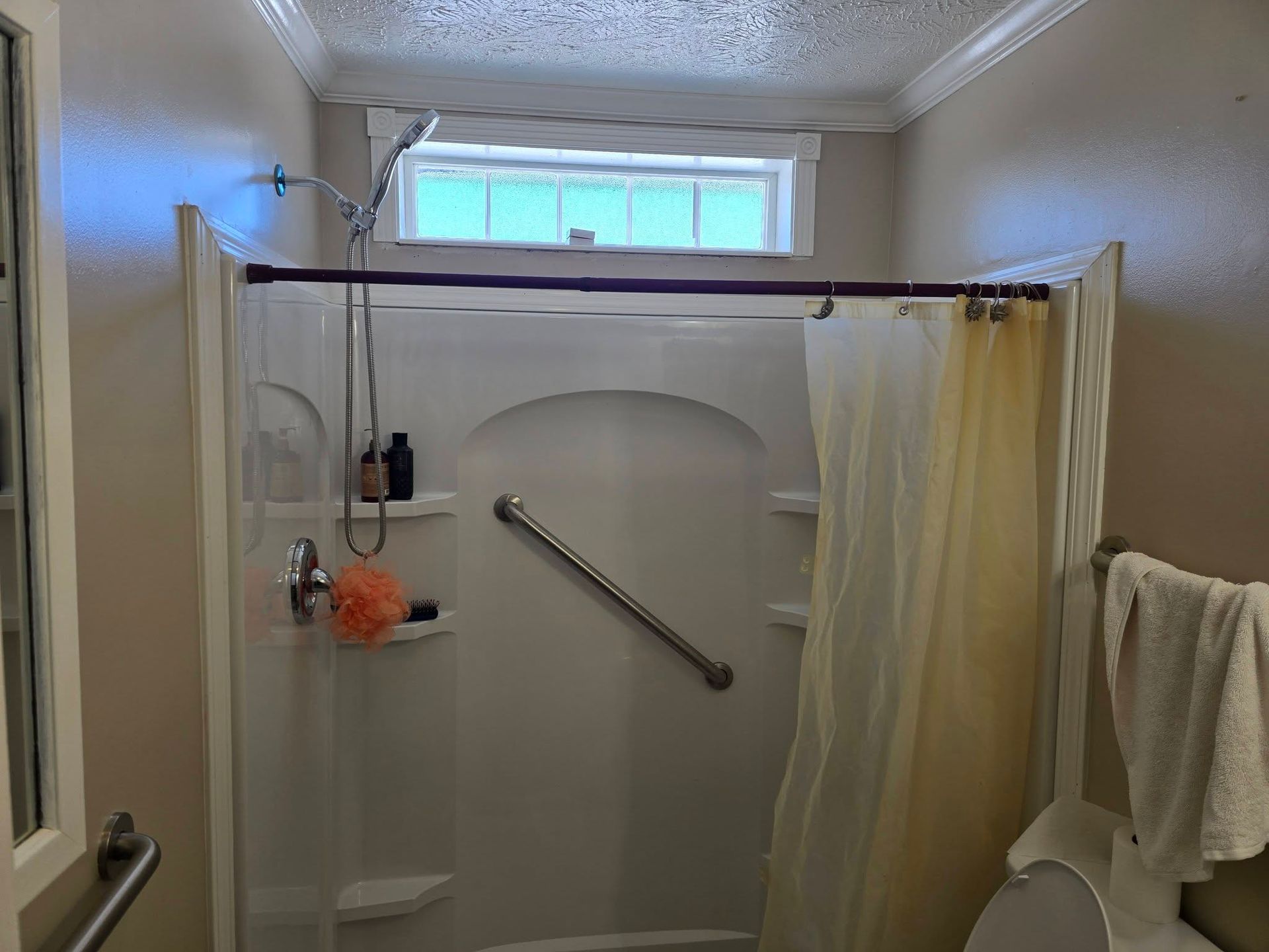 A shower stall with a yellow curtain, grab bar, handheld showerhead, and a small rectangular window above the unit.