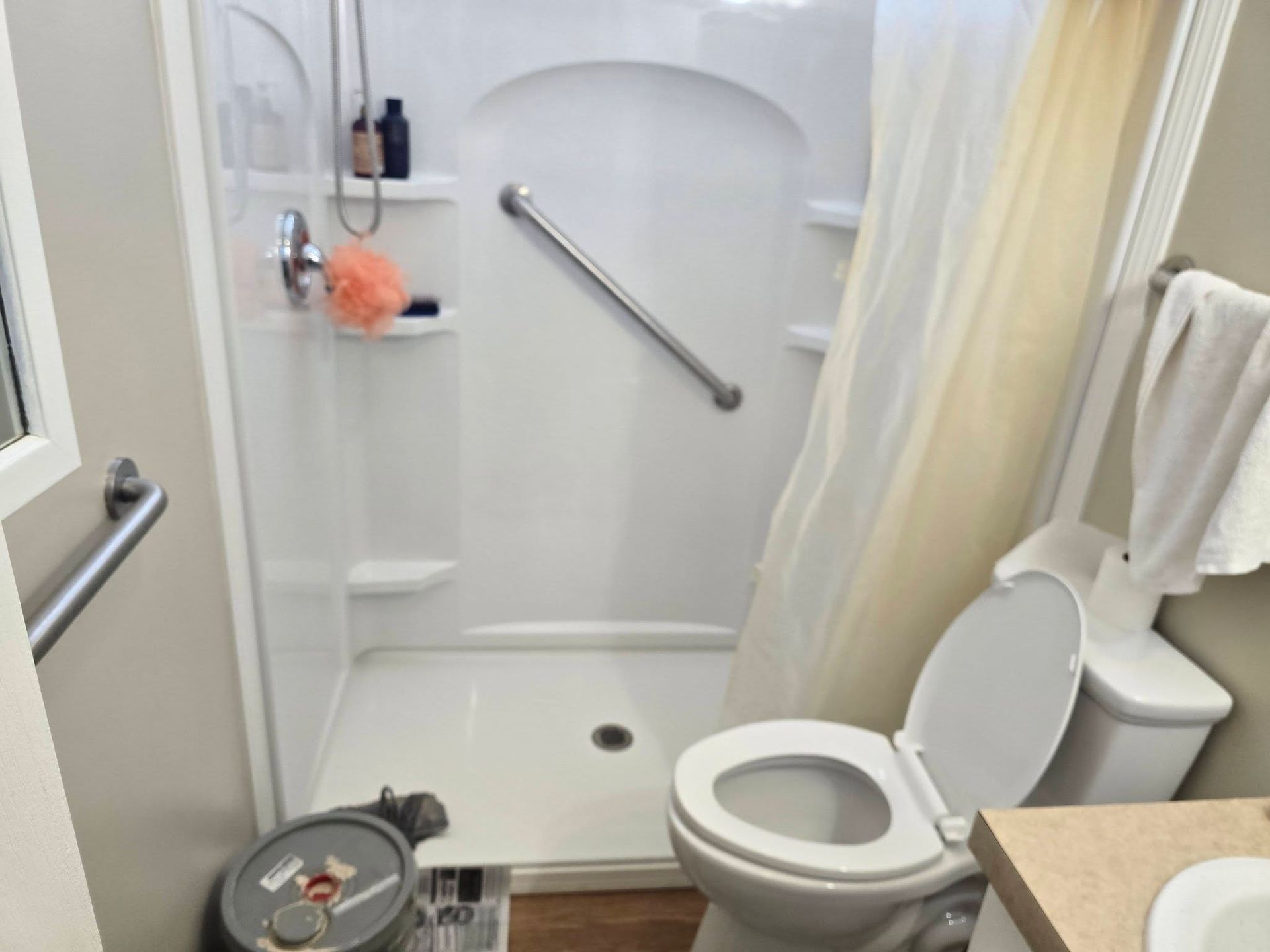 A bathroom featuring a shower stall with a grab bar, a white toilet, and a grab bar on the adjacent wall.
