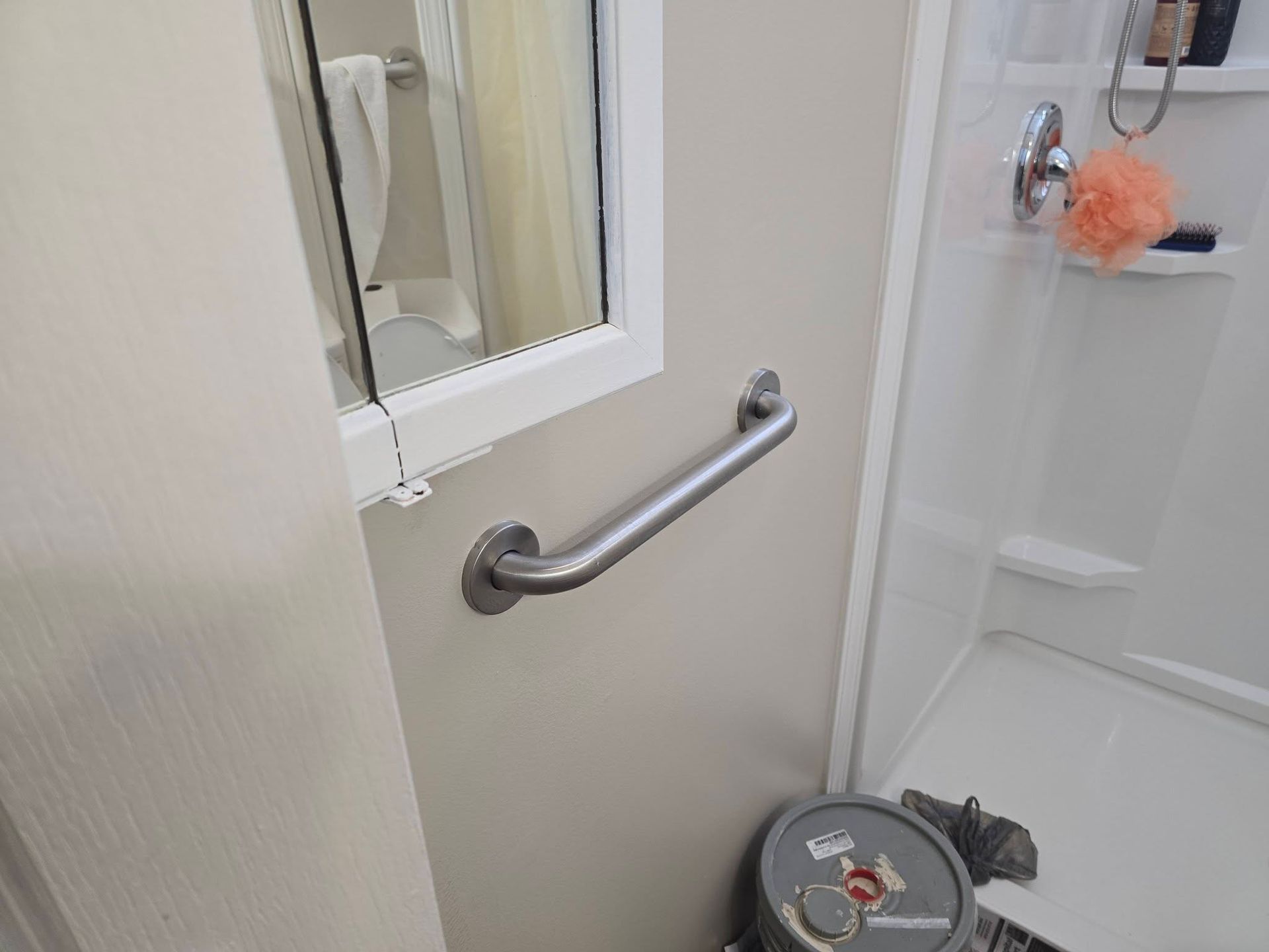 A metal grab bar mounted on a beige wall next to a shower enclosure in a bathroom.