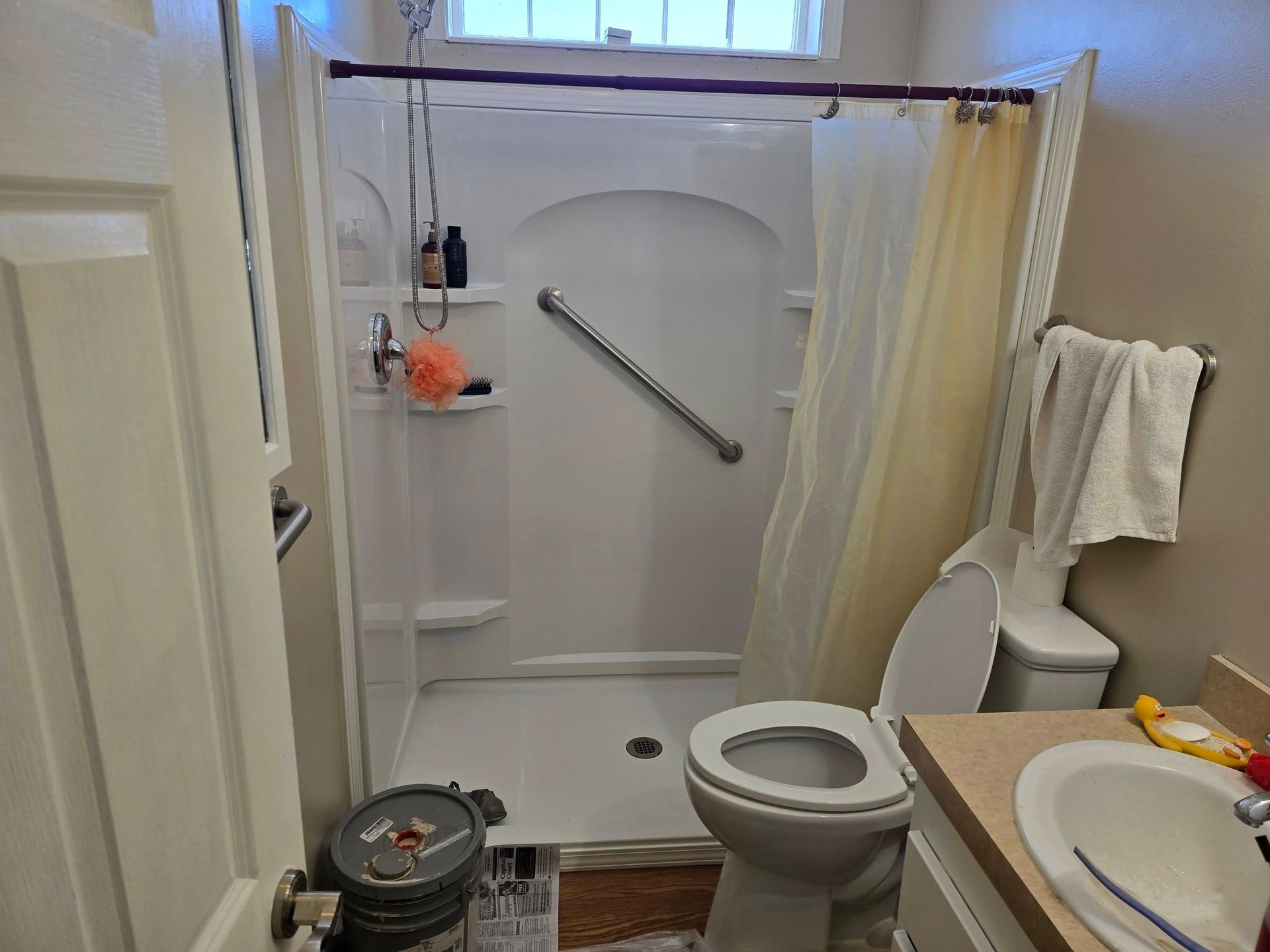 A small bathroom featuring a walk-in shower with a grab bar, a white toilet, and a vanity sink.