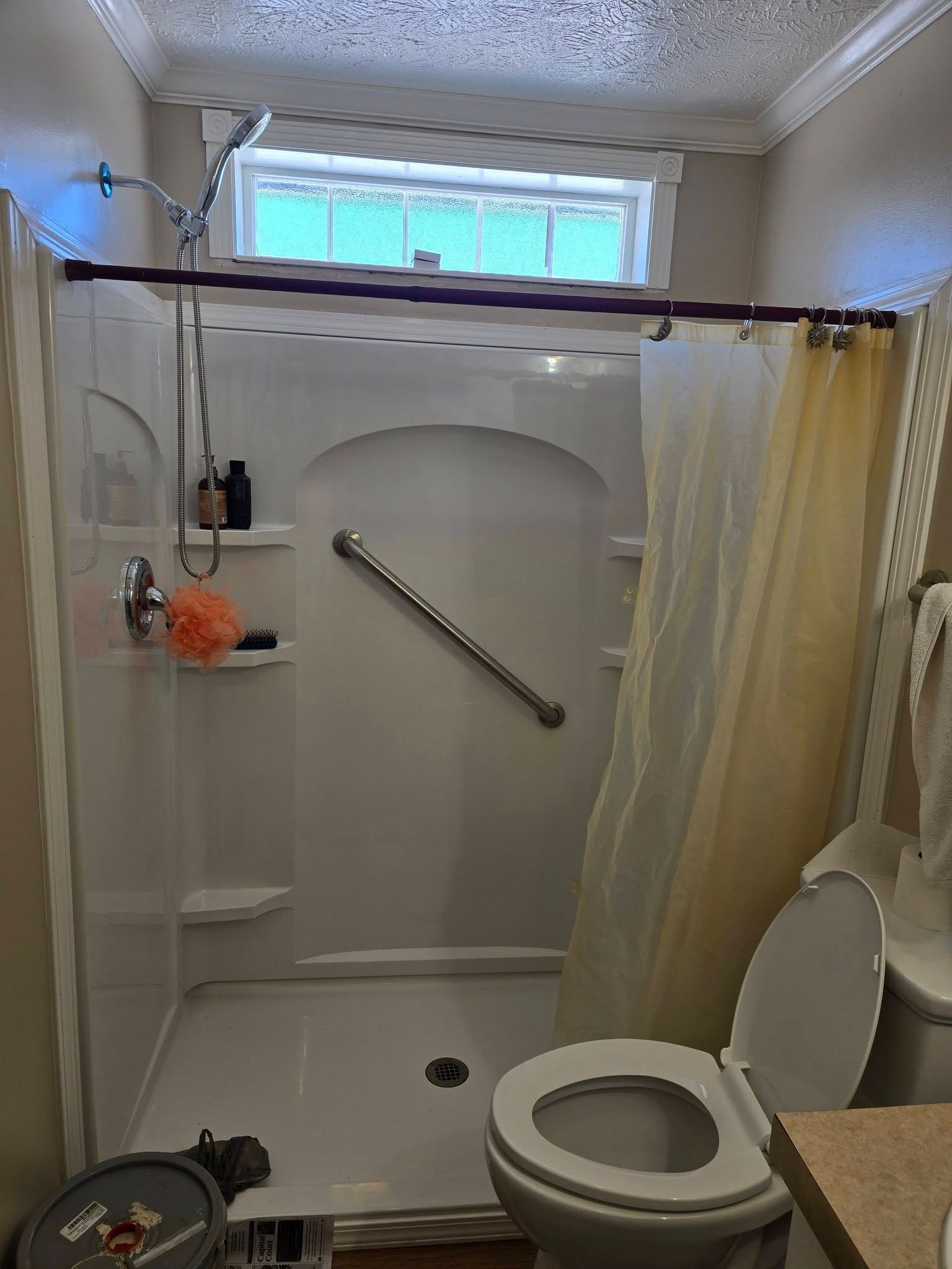 A bathroom featuring a white walk-in shower stall with a diagonal grab bar, shower curtain, and an adjacent toilet.