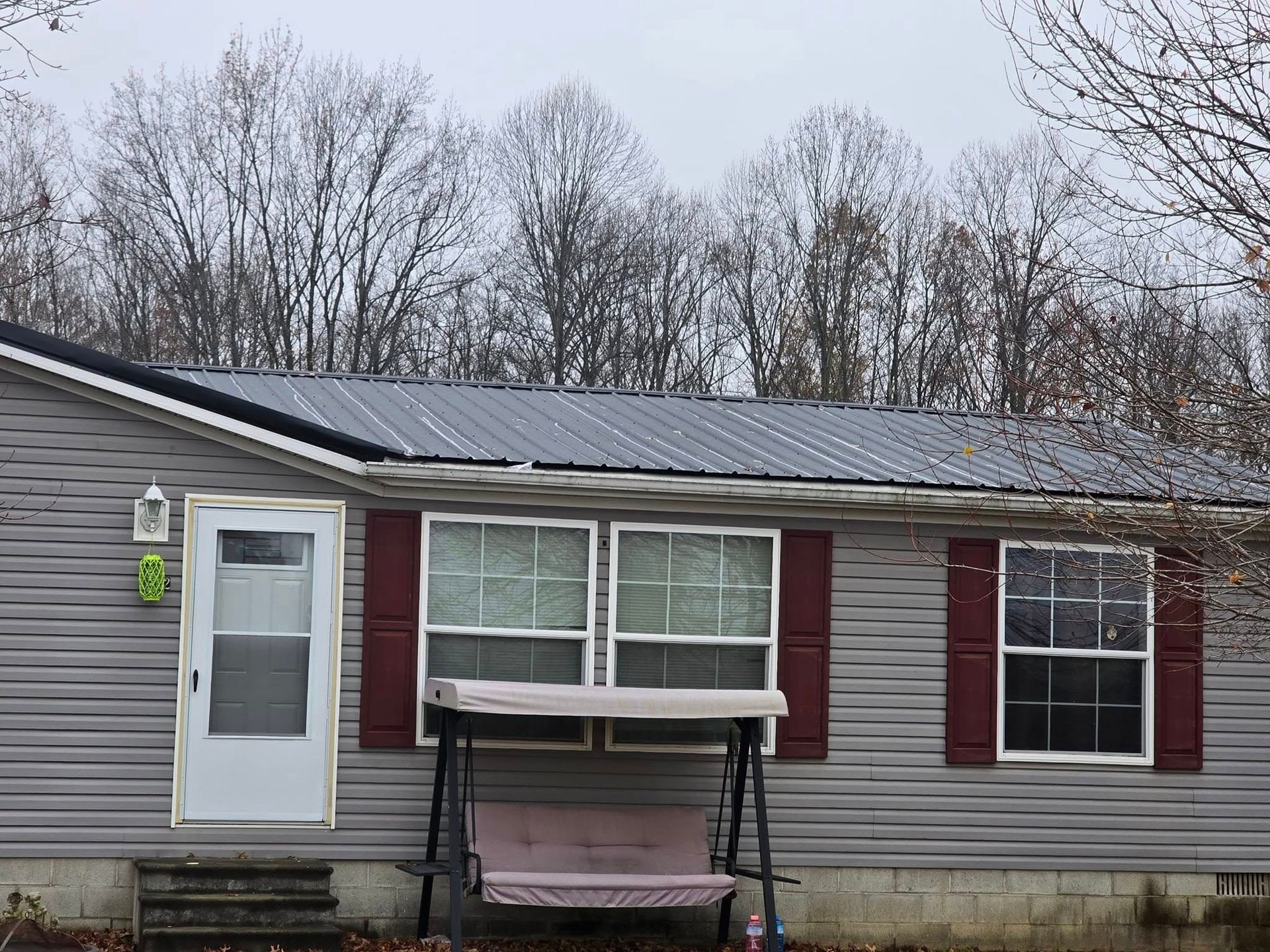 A light gray house with a metal roof and maroon shutters, featuring a porch swing in front of two windows.