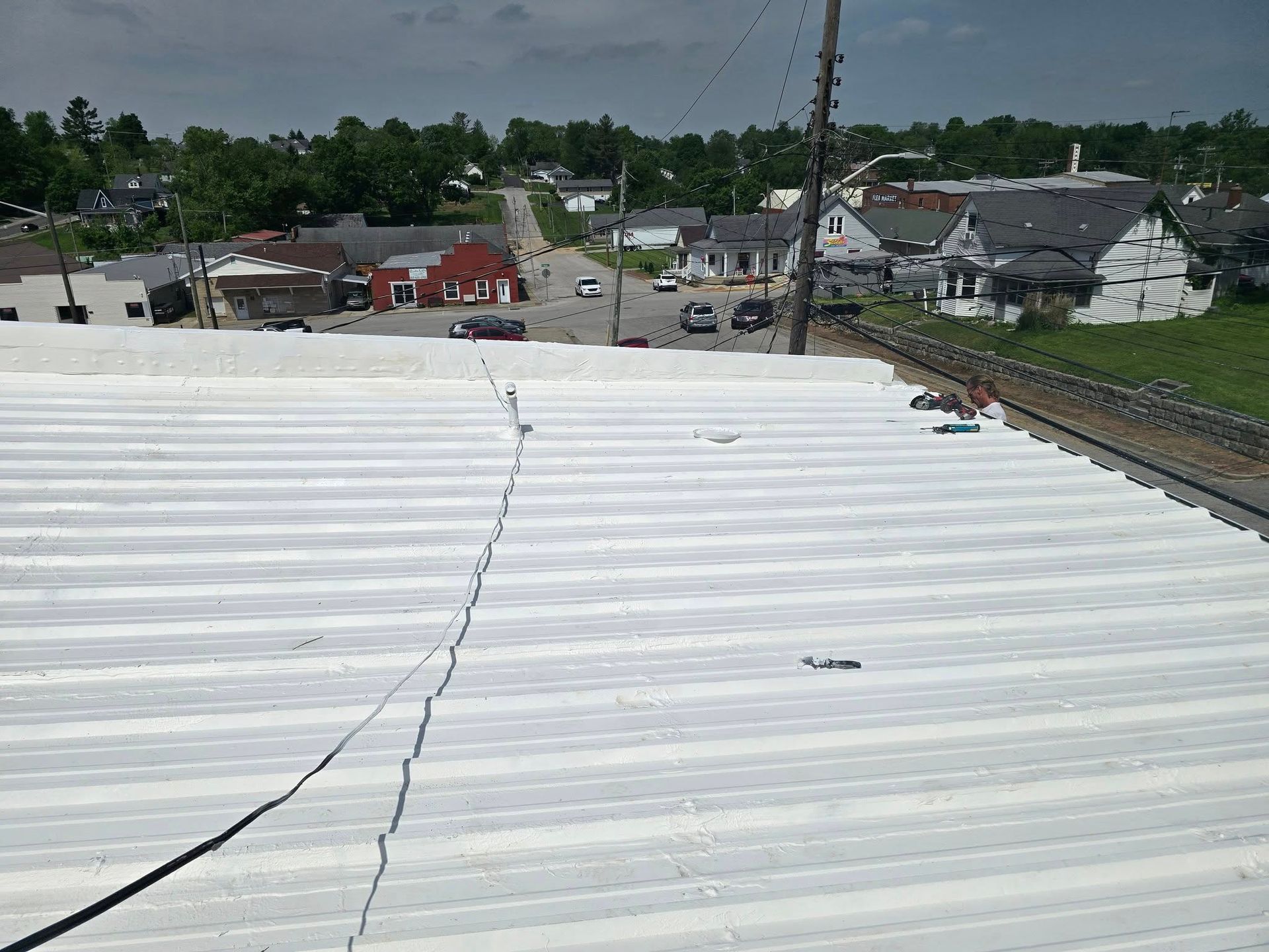 A white metal roof overlooking a small town street with homes and trees under a cloudy sky.