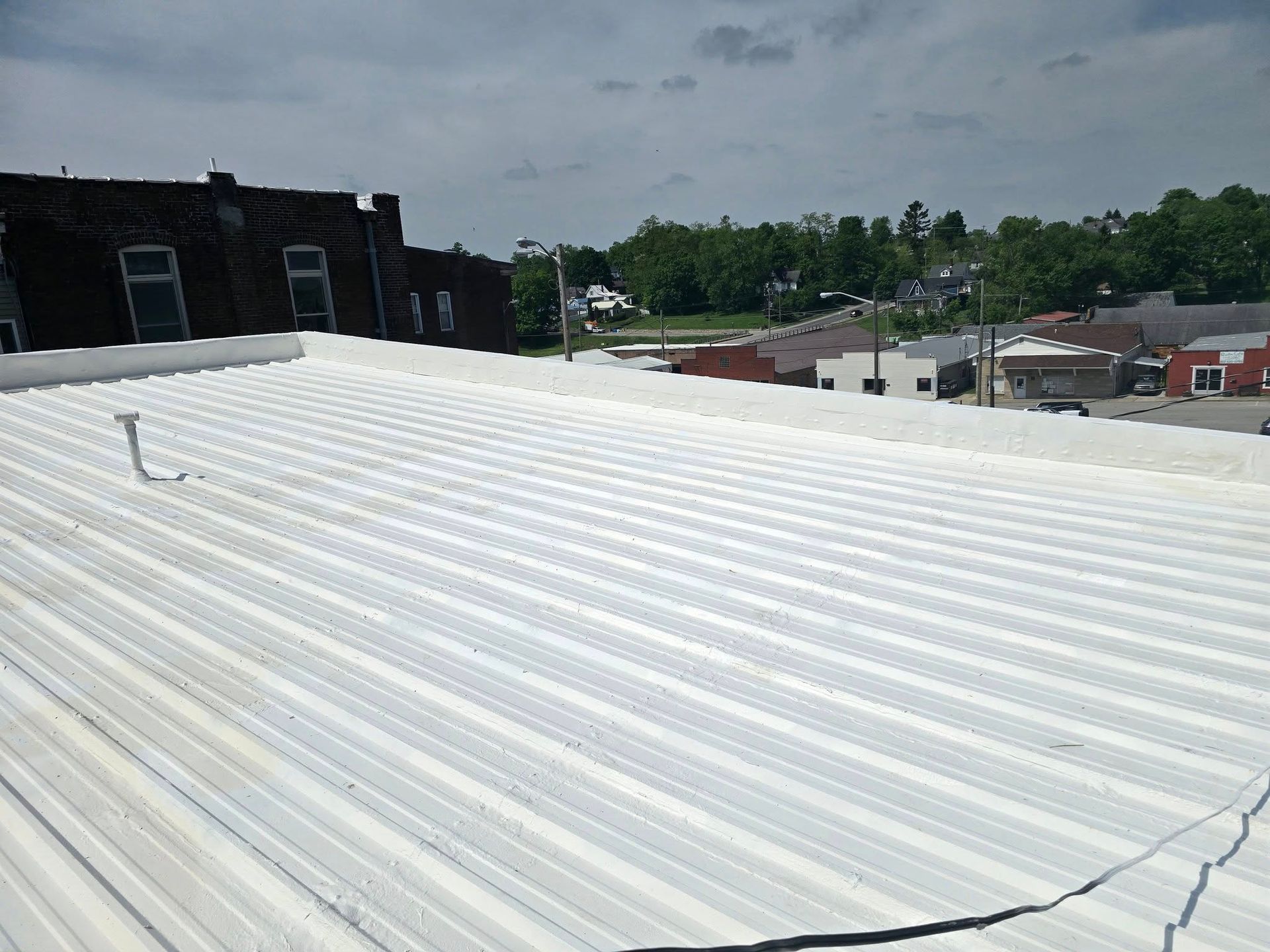 A high-angle view of a white, corrugated metal roof on a commercial building, overlooking a small town under a cloudy sky.