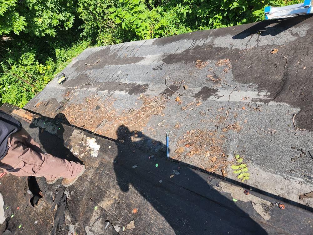 A person stands on a weathered, debris-covered roof next to a damaged section with exposed wood grain.