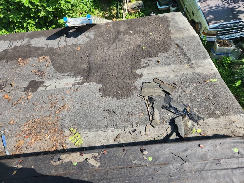 A weathered, damaged flat roof showing patches of peeling roofing material and debris in an outdoor setting.