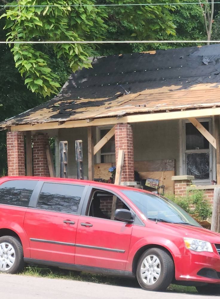 A red minivan parked in front of a house with a partially demolished roof and scaffolding.