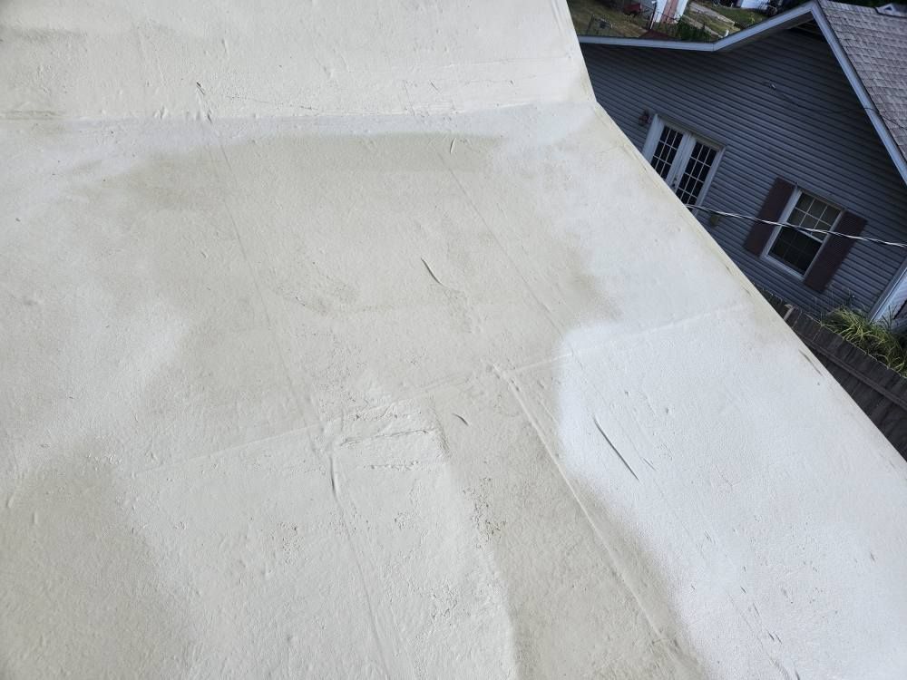 A close-up view of a light-colored, slightly worn flat roof surface with a dark house visible in the background.