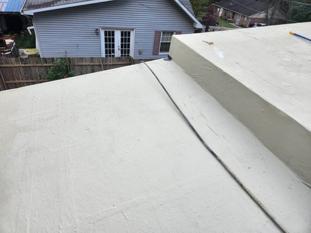 A slightly angled view of a light-colored flat roof with a visible seam, overlooking a neighboring gray-sided house.