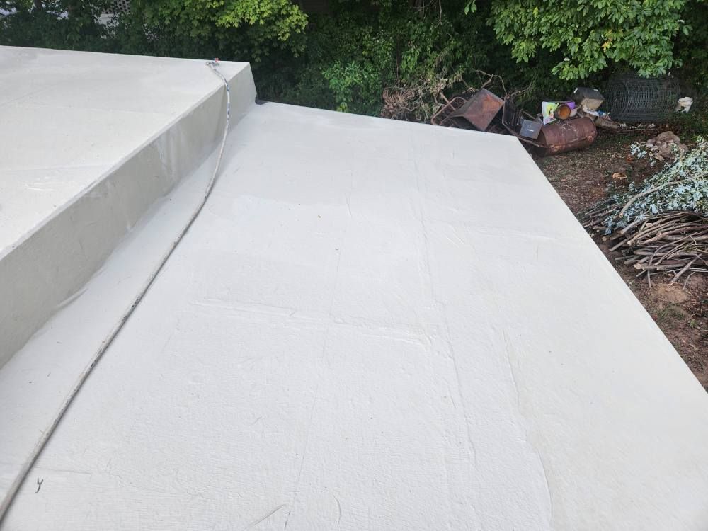 A freshly applied, light-colored waterproof coating covering a flat roof section with a raised curb.