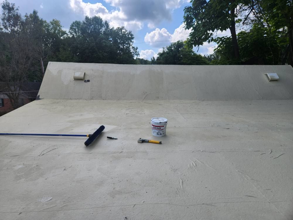 A wide, low-angle shot of a tan-colored flat roof under a blue sky, featuring a broom, a paint can, and a tool.