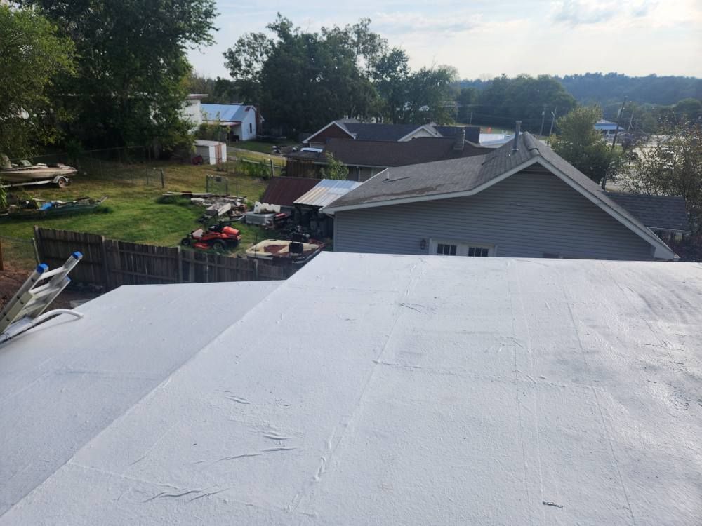 A view from a rooftop looking out over a grassy backyard, a neighboring house, and a treelined horizon.