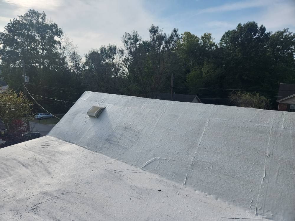 A white, coated rooftop with a small ventilation hood, set against a backdrop of trees and a clear sky.