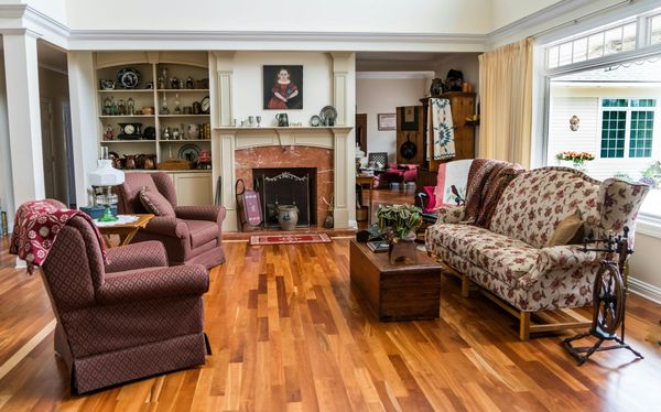 A living room with wooden floors, floral furniture, a fireplace, and bookshelves, viewed from the doorway.