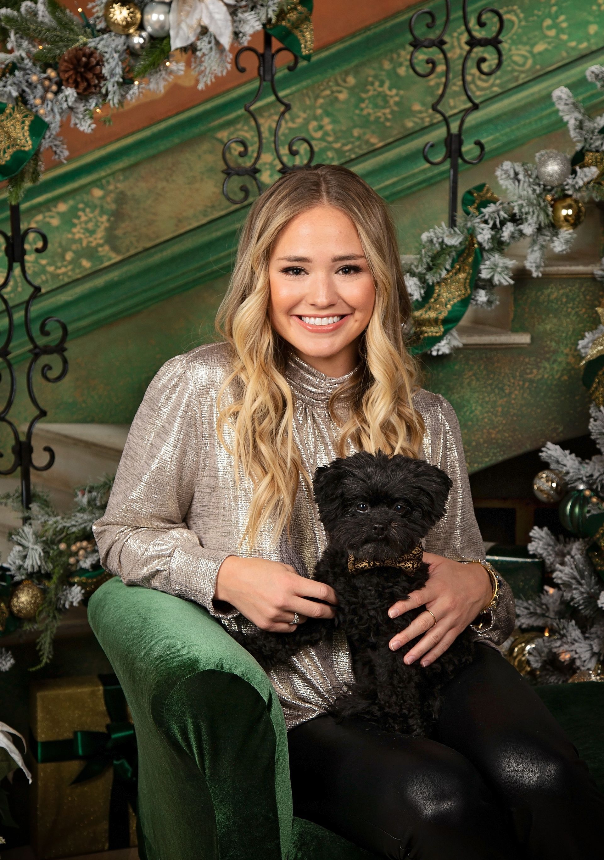 A woman is sitting in a chair holding a black dog in front of a Christmas tree.