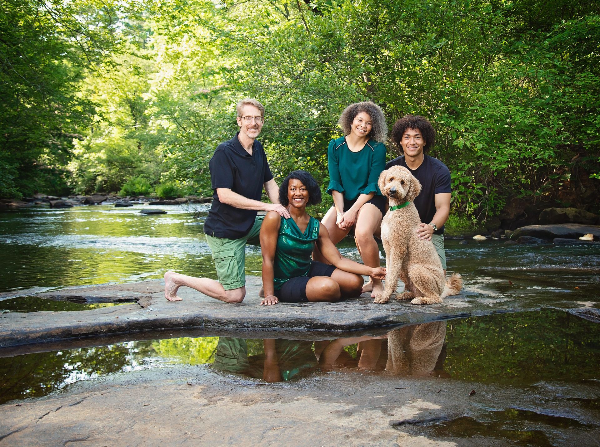 A family and their dog are sitting on a rock in a river.