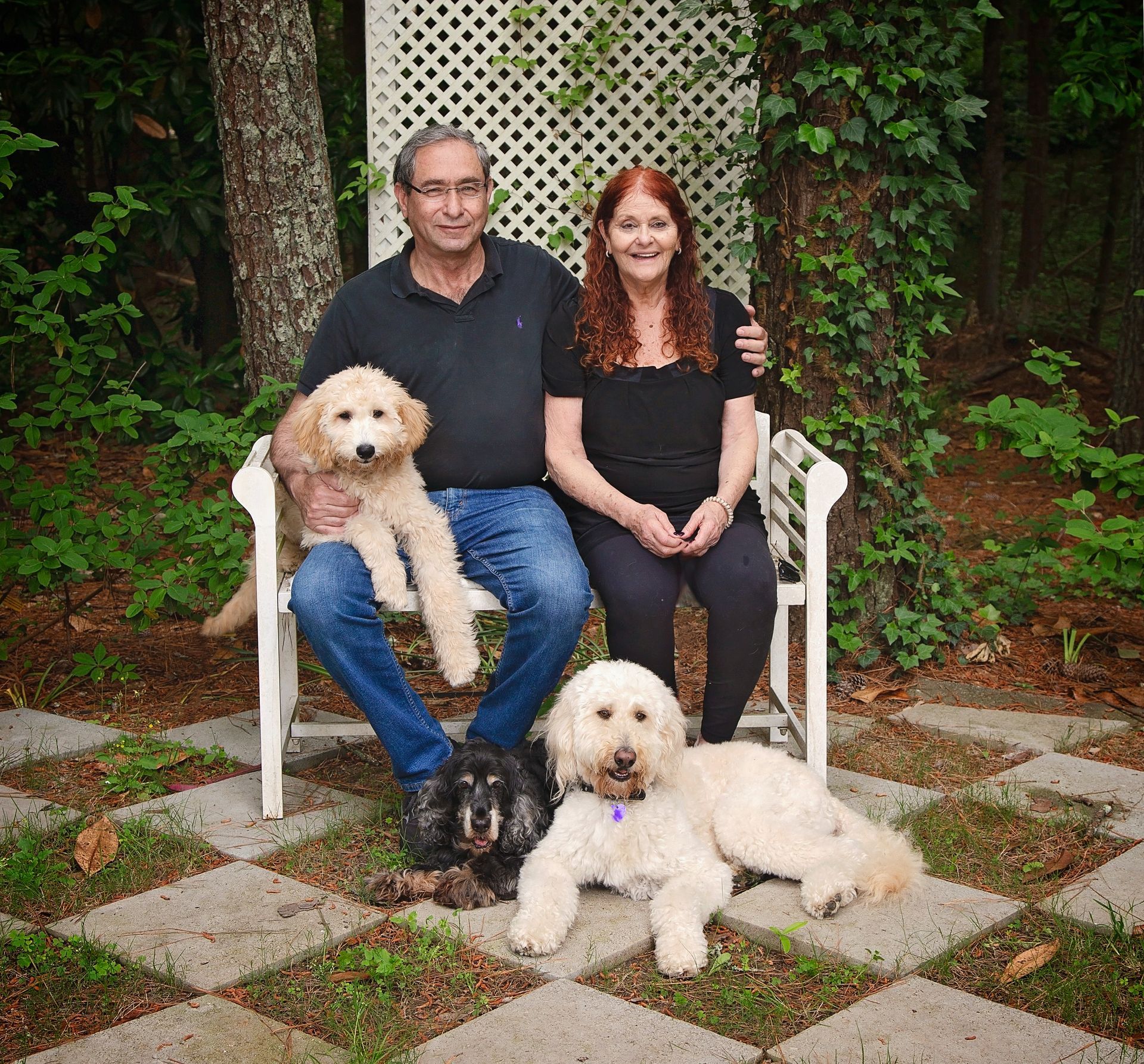 A man and woman are sitting on a bench with two dogs.