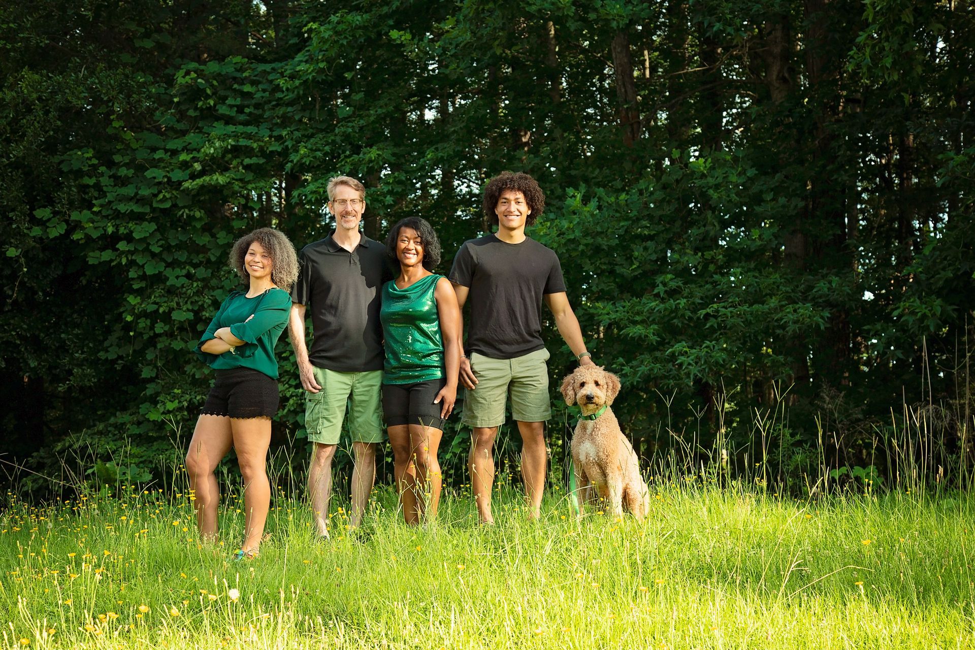 A beautiful family and their dog are standing in a grassy field.