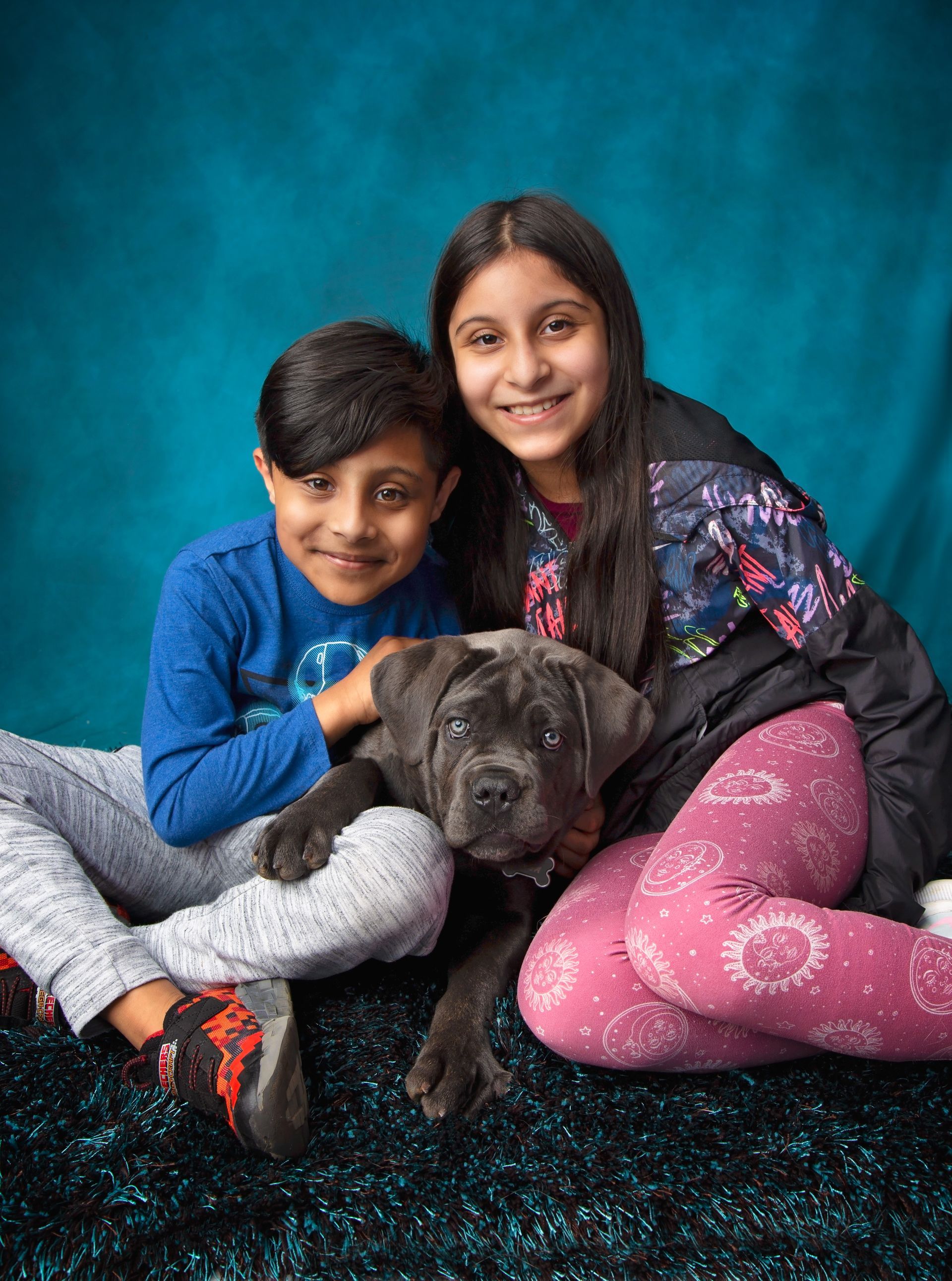 A boy and a girl are sitting on the floor with a dog.