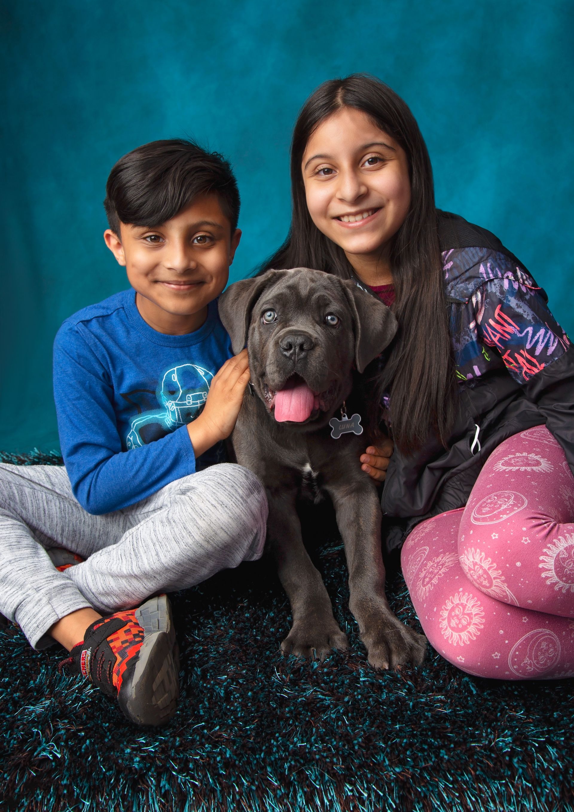 A boy and a girl are sitting on the floor with a dog.
