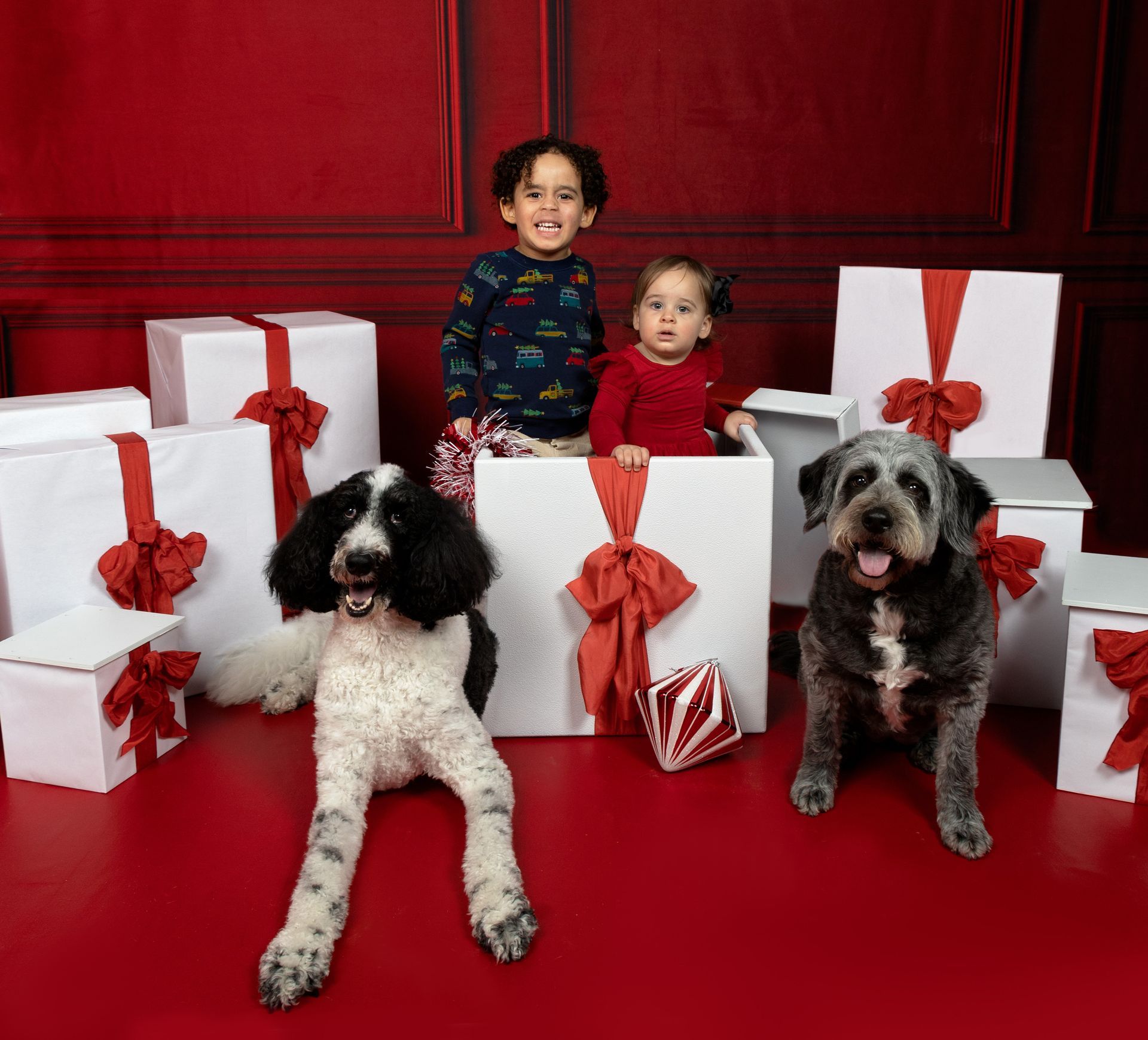Two children and two dogs are posing for a picture in front of christmas presents.