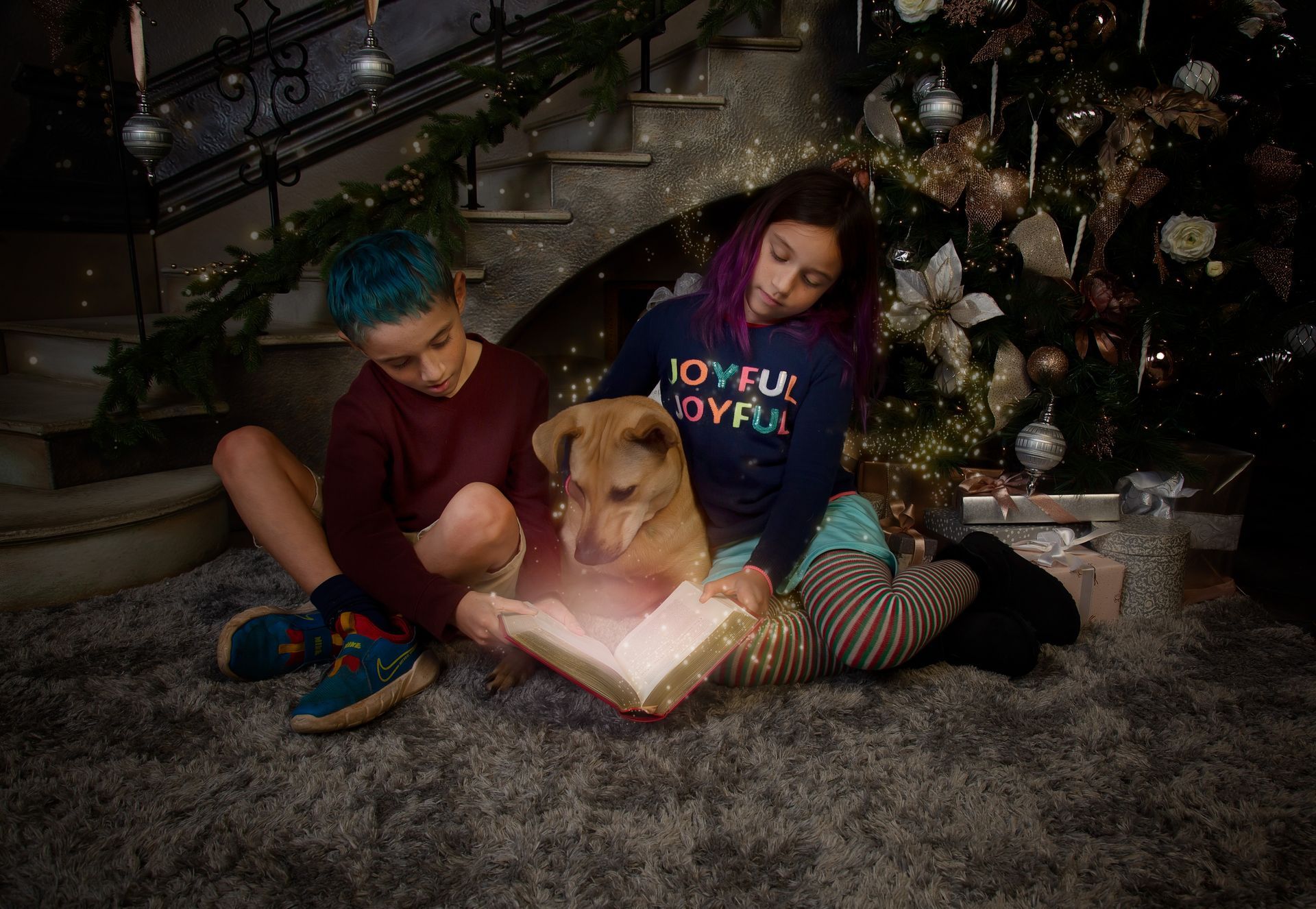 A boy and a girl are sitting on the floor reading a book to their dog.
