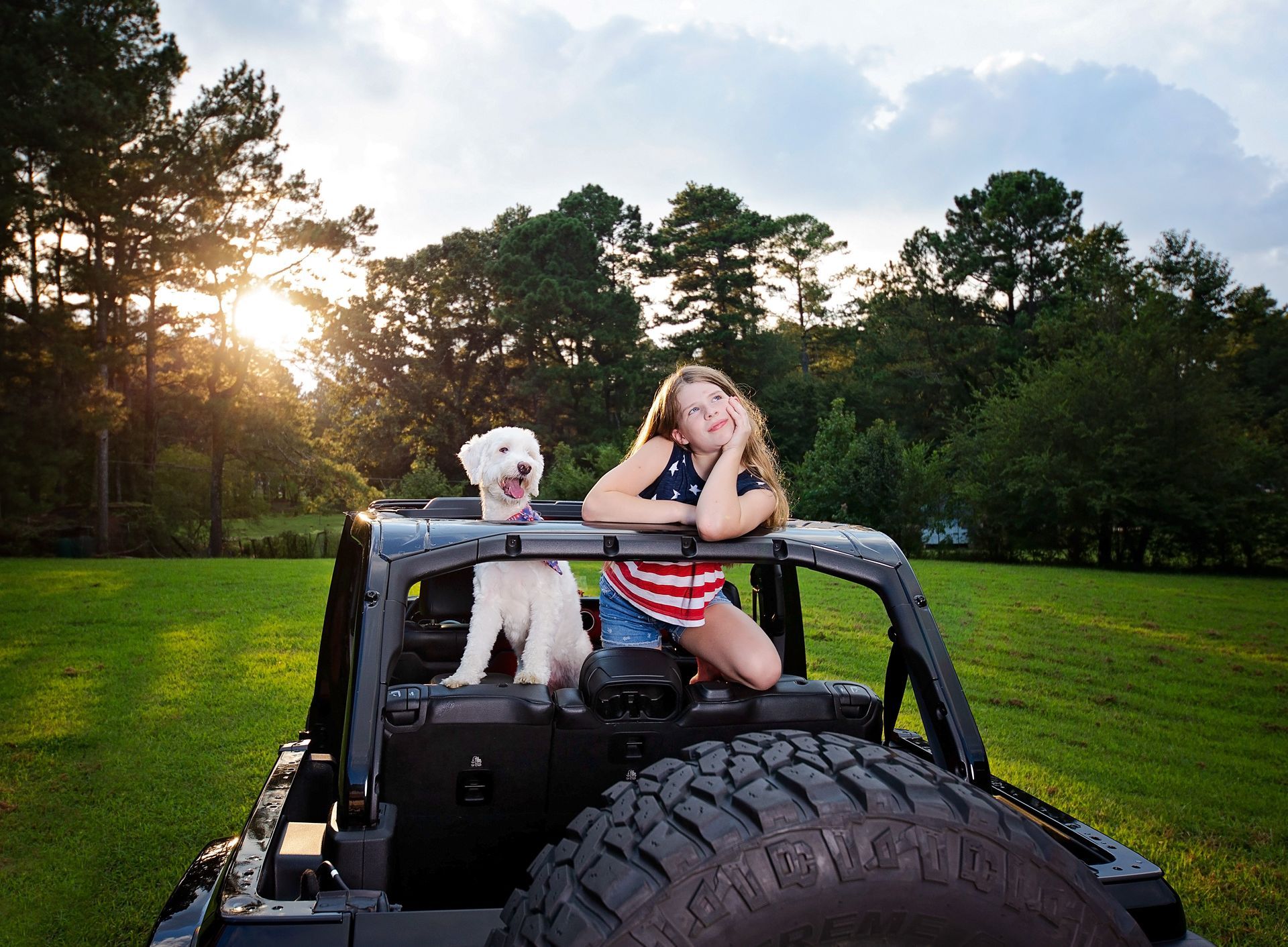A girl and her dog are sitting in the back of a jeep.