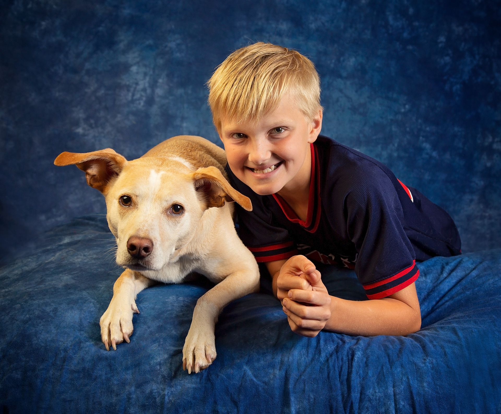 A boy is laying on a blue blanket next to a dog.
