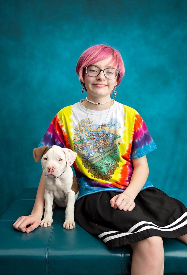 A smiling girl with pink hair is sitting on a bench with a puppy.