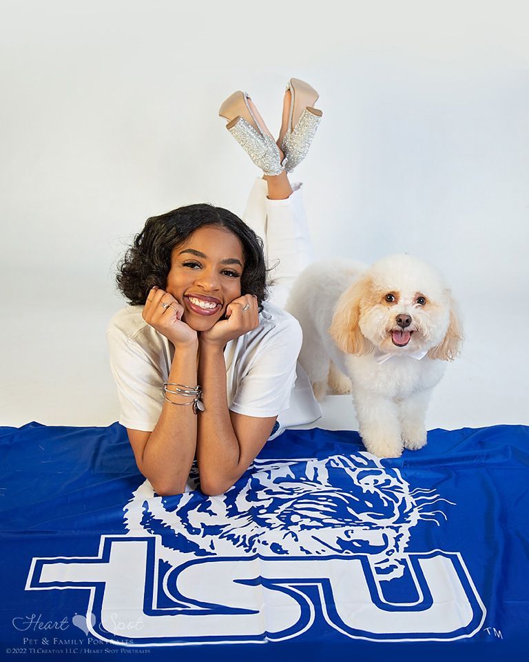 A young woman is laying on a blue LSU school flag next to a small white dog.