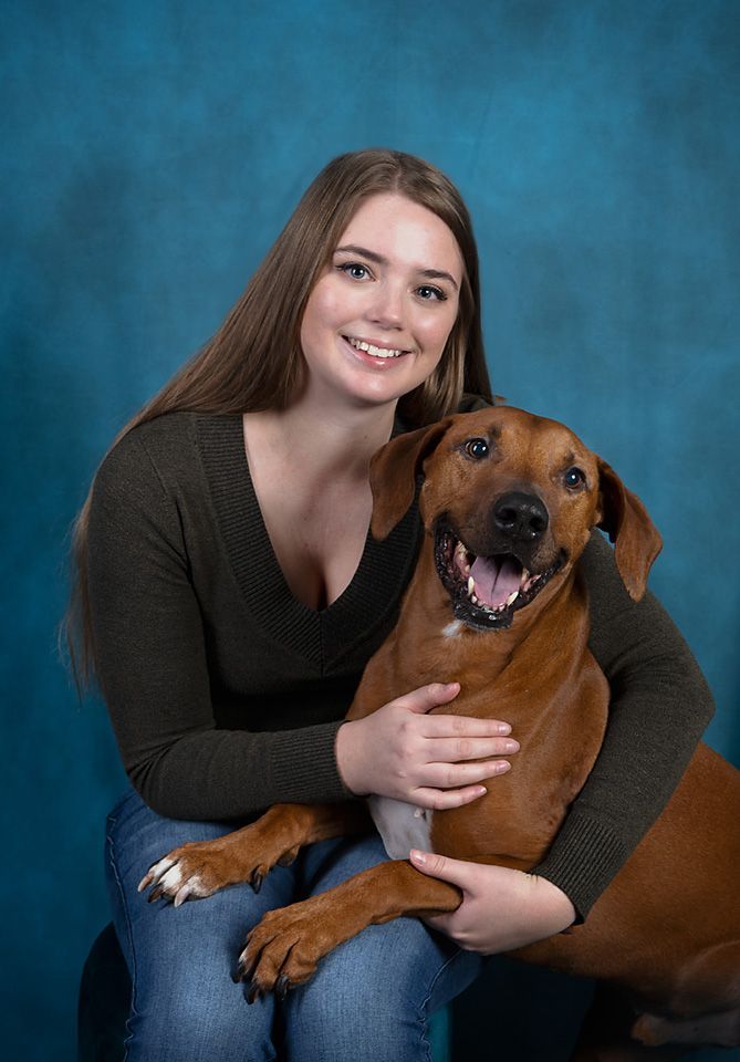 A woman is sitting next to a brown dog on a blue background.