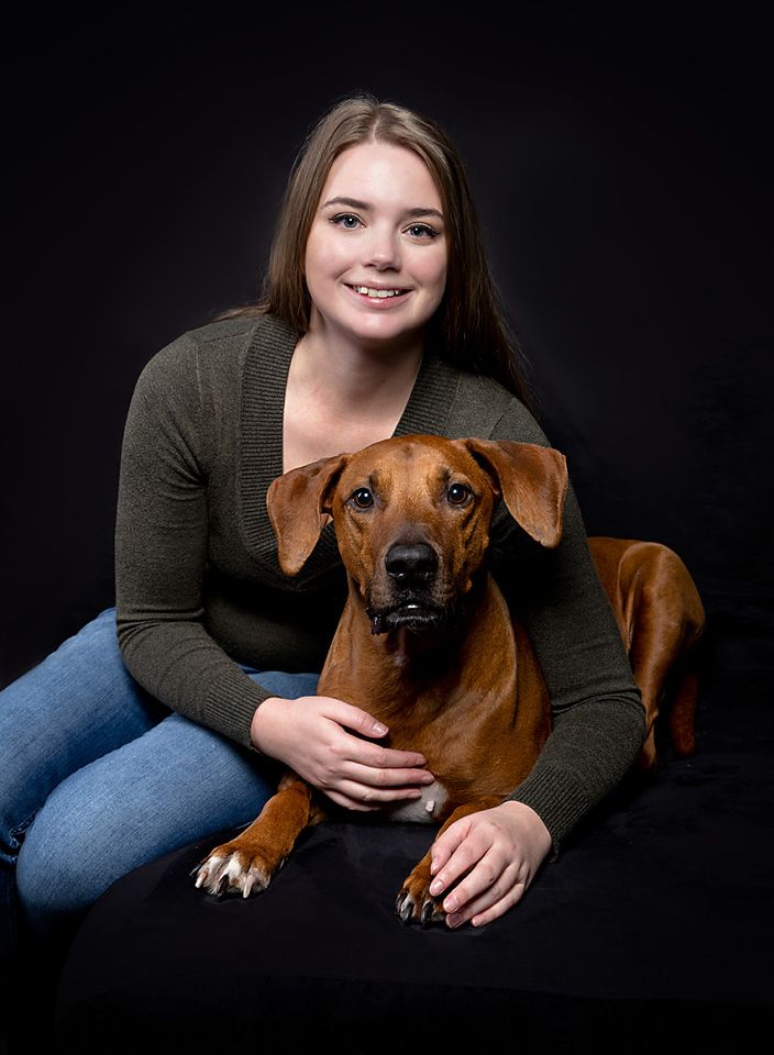 A woman is sitting next to a brown dog on a black background.