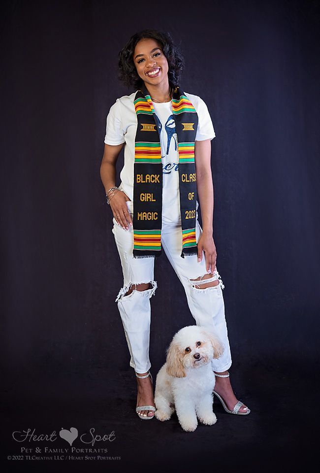 A woman in a graduation cap and gown is standing next to a small white dog.