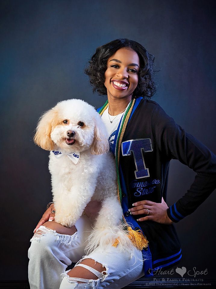 A graduating high school senior girl  is sitting with her small white dog on her lap.