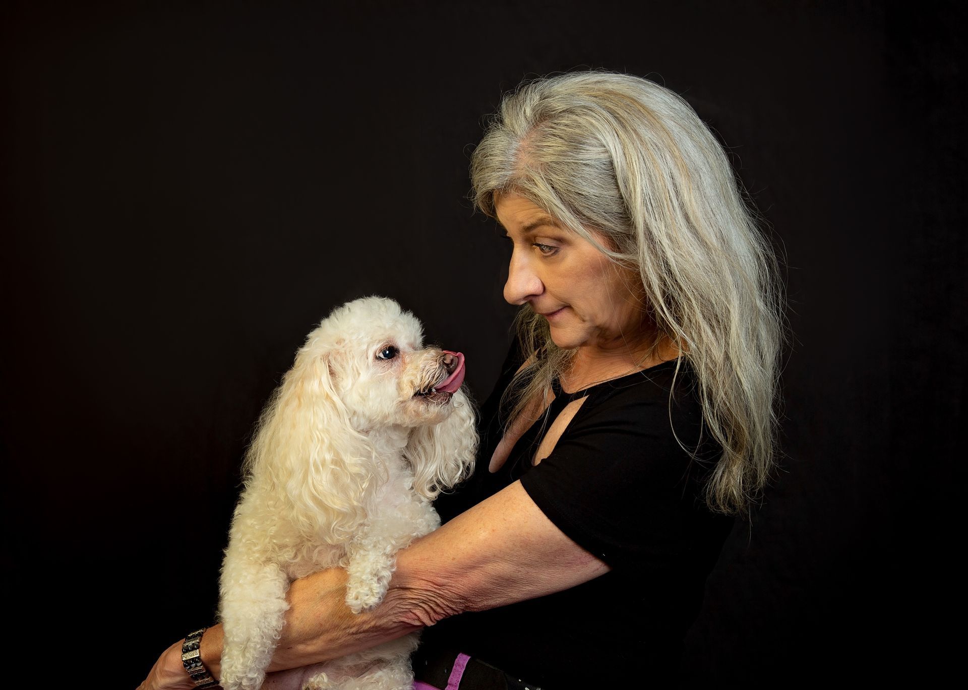 A woman is holding a small white dog in her arms as they look lovingly into each other's eyes.