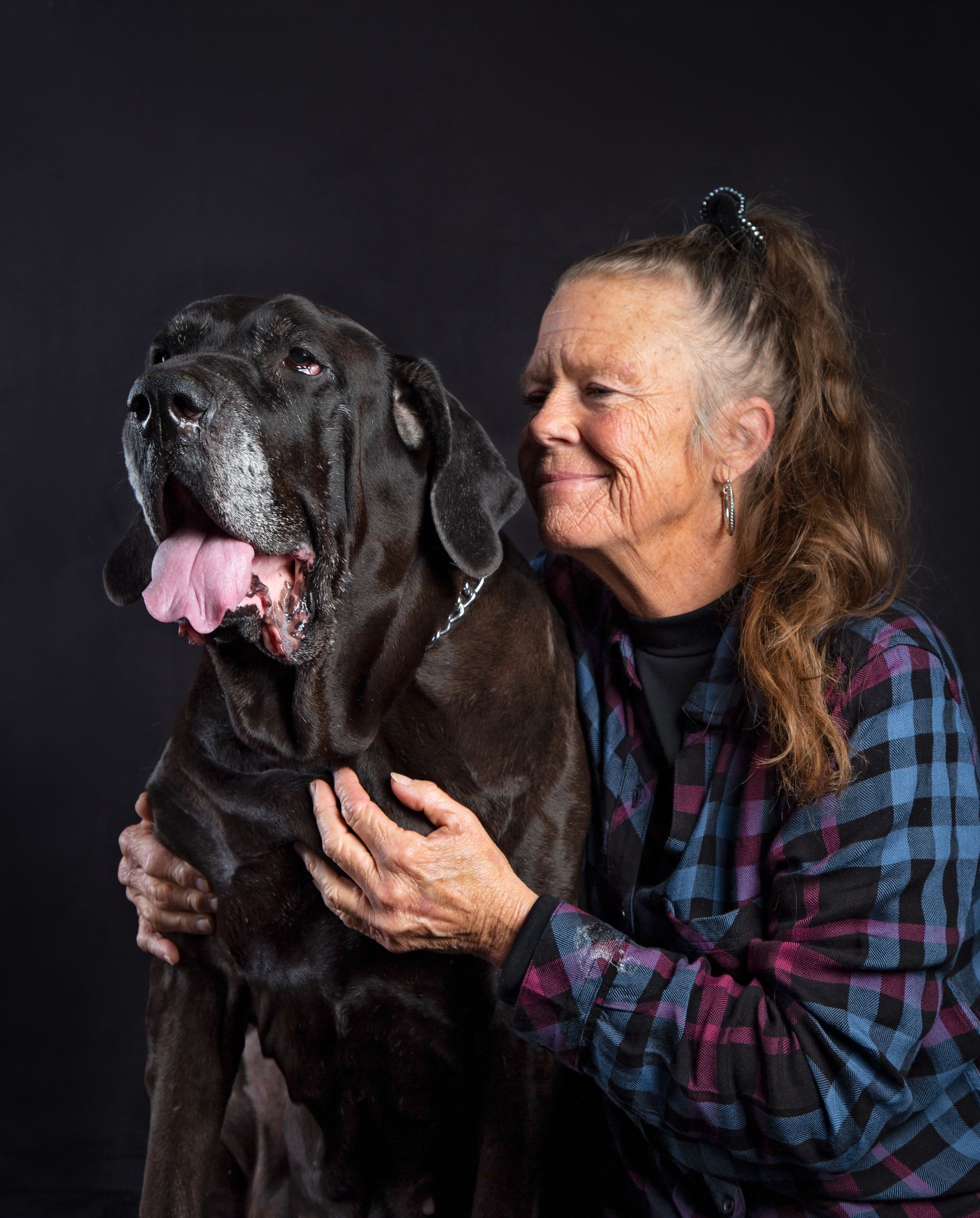 A woman is hugging a large black Mastiff dog in her arms.