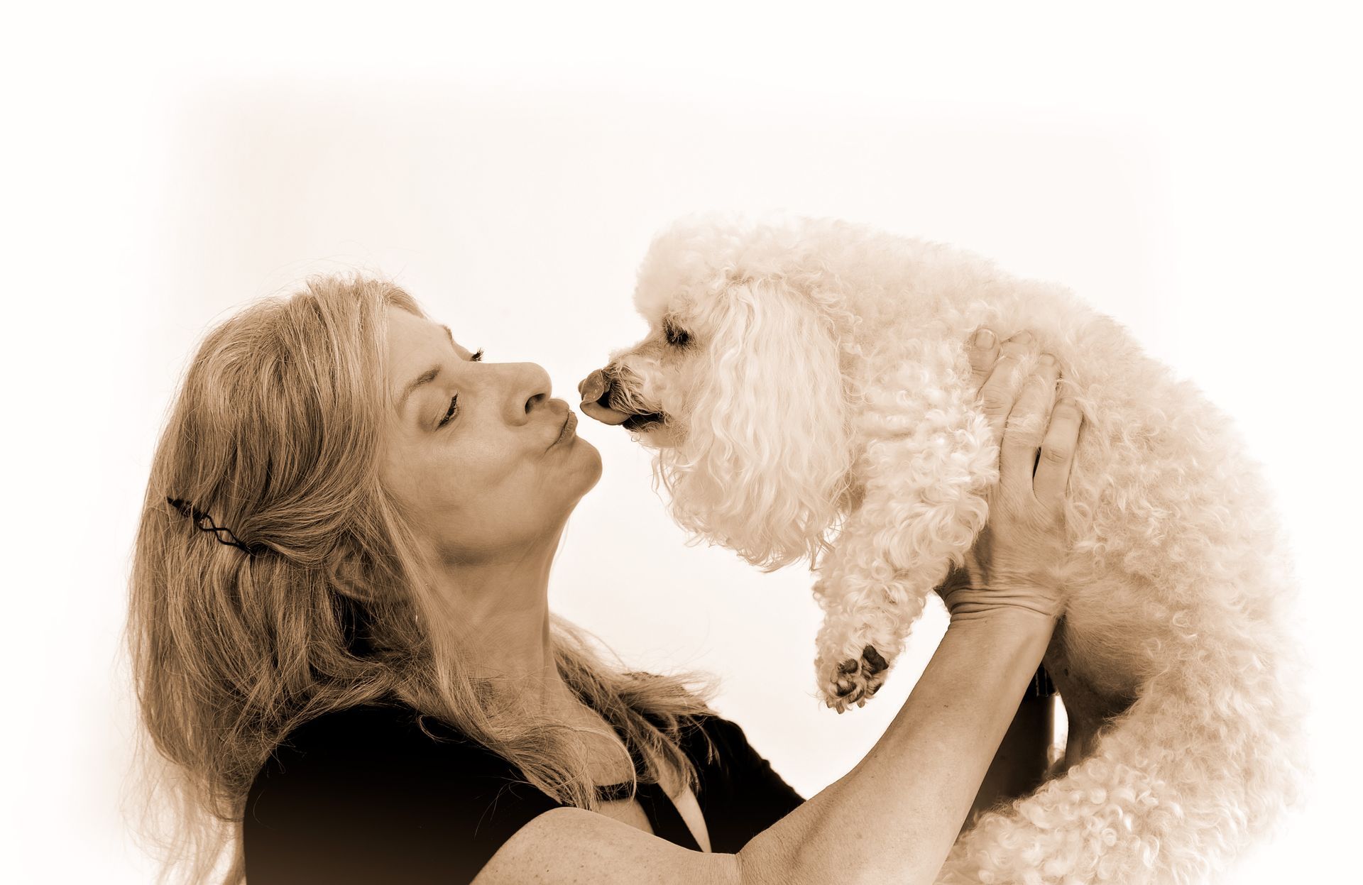 A woman is kissing a small white poodle on the nose in a black and white photo.